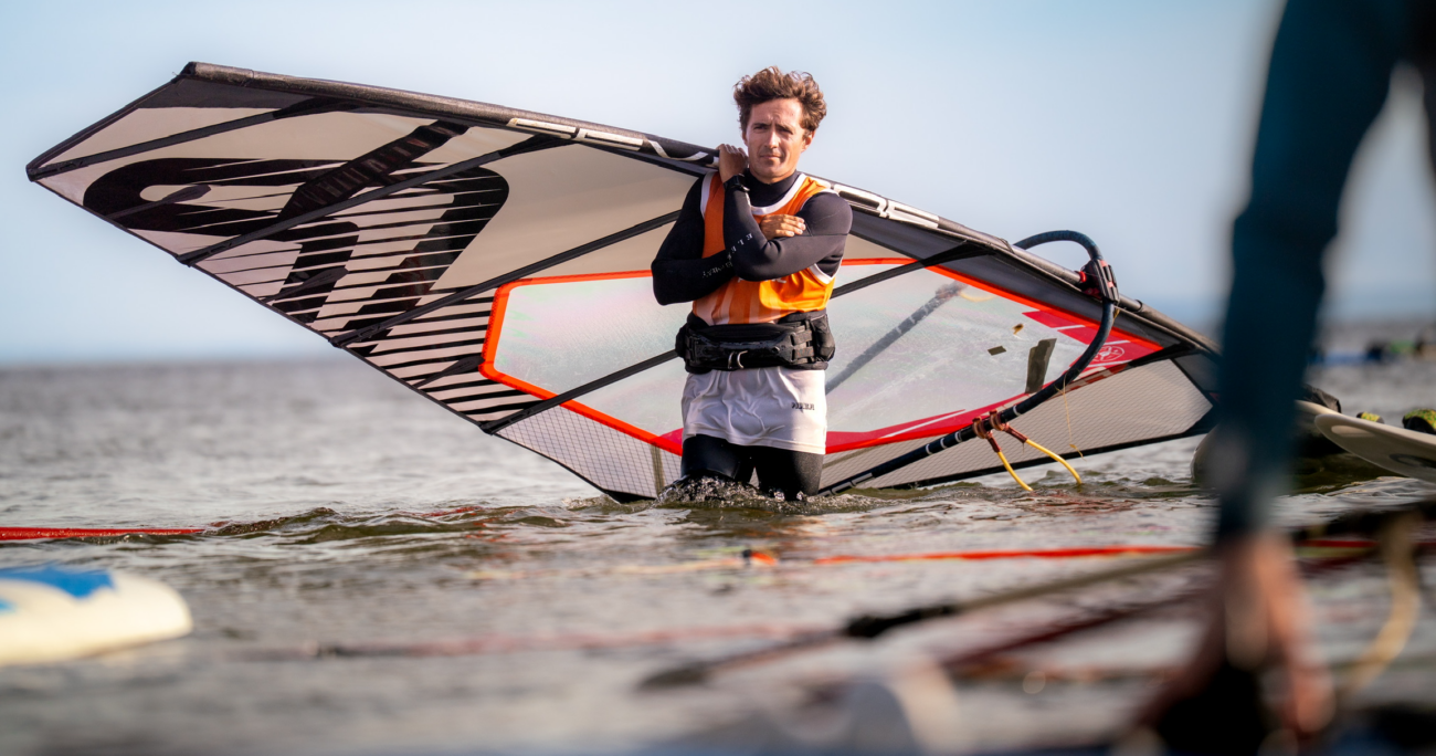windsurfing, windsurfer stojący w wodzie z żaglem