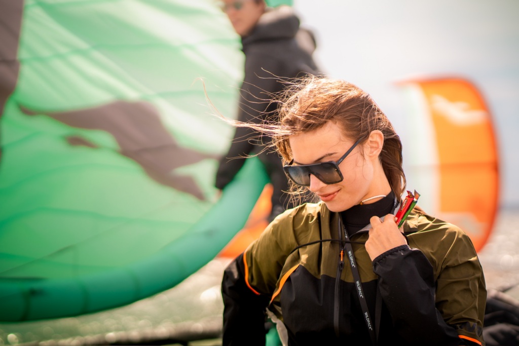 Kobieta na tle pędników windfoilowych i kitesrufingowych, wiatr we włosach, Surfcamp